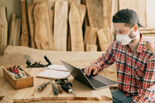 man on woodshop with tools and laptop